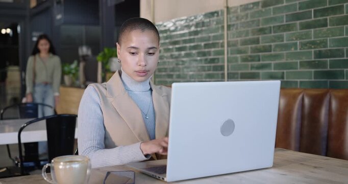 Mid-adult Asian woman typing on laptop at cafe, pausing, speaking into phone to reference laptop