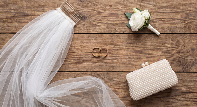 An elegant bridal flat lay composition featuring a sheer white tulle veil paired with a beaded evening clutch bag and a white rose corsage