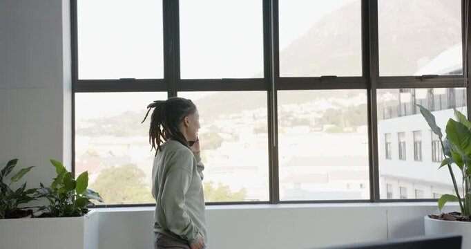 African-American nonbinary adult green top standing left window answering mobile call, copy space