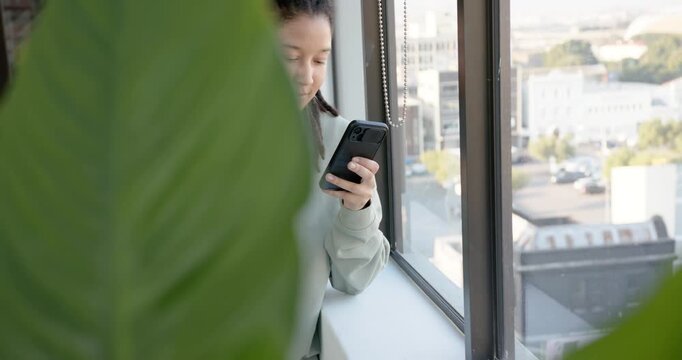 African American nonbinary person shifting, leaning on sill with smartphone, scrolling and smiling