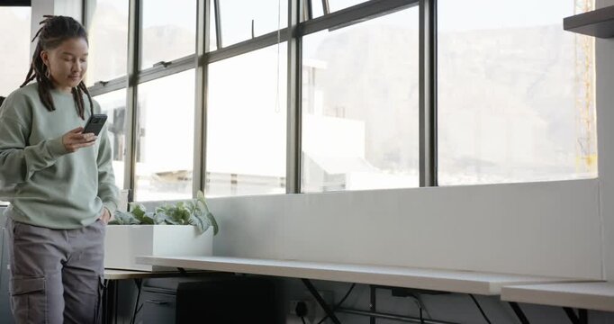 Nonbinary entering office propping leg on bench, sitting, scrolling phone checking texts