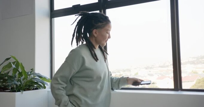 African American nonbinary adult in sweater by window ending call placing phone on sill reflecting
