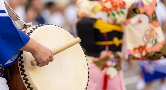 Close-up of a drummer in festive festival clothing holding wooden bachi sticks while energetically beating a large traditional Japanese taiko drum