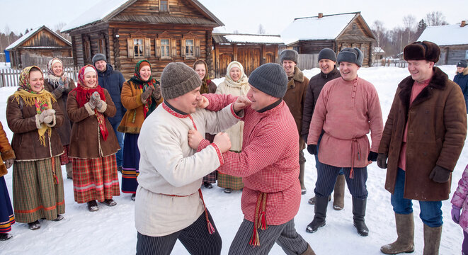 Group of men in traditional winter coats and caps engaged in friendly folk fist fight and wrestling match in deep snow surrounded by cheering spectators