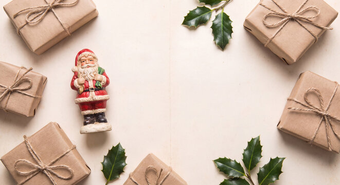A top down view of Christmas presents wrapped in brown kraft paper tied with twine alongside fir sprigs and vintage Santa decoration.
