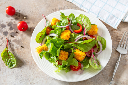 Summer fresh vegetable salad with crispy breaded feta cheese on a textured stonesurface. Tasty appetizer ready to eat.