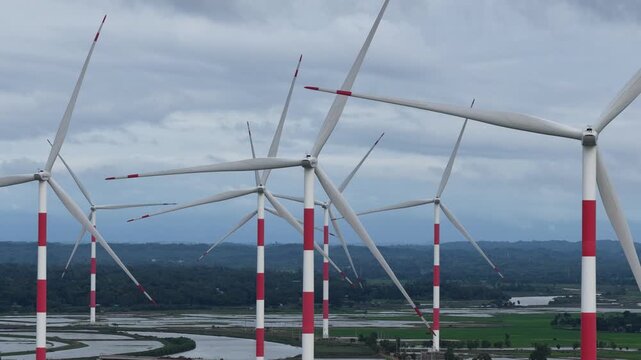 Aerial view of the Cox's Bazar 60 MW Wind Power Plant with large turbines set against a landscape of green fields and water in Cox's Bazar, Chittagong Division, Bangladesh.