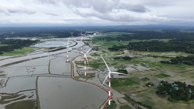 Aerial view of the Cox's Bazar 60 MW Wind Power Plant featuring white and red wind turbines standing in flooded fields and rural landscape in Cox's Bazar, Chittagong Division, Bangladesh.