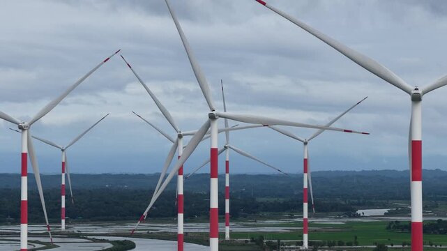 Aerial view of Cox's Bazar 60 MW Wind Power Plant with large white and red turbines standing over green fields and waterways Cox's Bazar, Chittagong Division, Bangladesh.