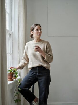 Smiling woman wearing a hearing aid standing by a bright window &ndash; Great for audiology promotions, inclusion campaigns, or health features