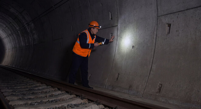 Safety inspector in high visibility jacket using flashlight to check dark subterranean subway tunnel and tracks