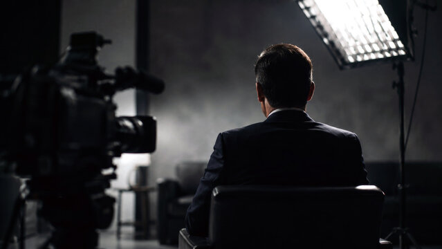 Businessman sitting with his back to the camera during a filmed studio interview with professional video and lighting equipment