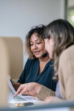 Two colleagues review a printed floor plan together, a woman speaking into a headset while a coworker points to a detail for property consulting