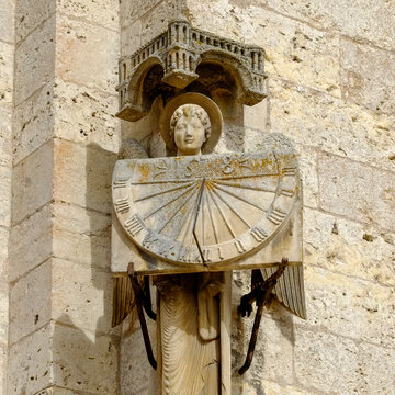 Carved stone sundial with a female figure on a cathedral wall