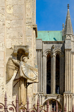 Stone statue holding a sundial with cathedral spires in the background