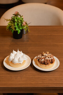 A dessert of meringue flakes and another of chocolate with a crispy coating on a wooden table.