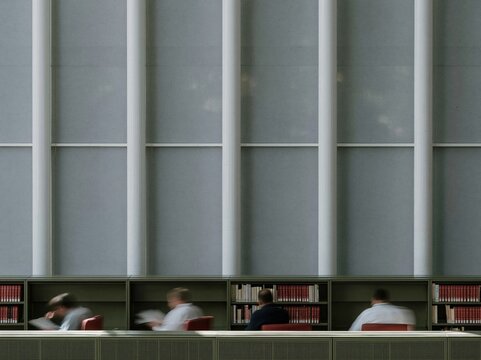 Blurred figures of readers in a library with green shelving, featuring smooth motion trails and neutral tones for education and literacy concepts