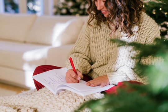 Woman in a chunky knit sweater writing in a notebook, a cozy and reflective scene for winter journaling and self-improvement campaigns