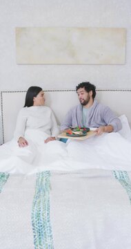 Vertical video: African American couple sitting in bed, man talking moving tray offering breakfast