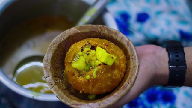 Close-up cinematic b-roll footage of serving hot spicy potato curry over a crushed deep-fried kachori in a traditional leaf bowl (dona), showcasing authentic Indian street food.
