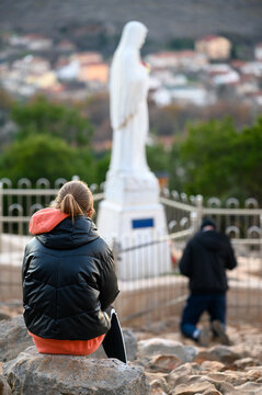 Tween girl praying at the statue of the Virgin Mary on Mount Podbrdo,  the Apparition Hill overlooking Medjugorje, Bosnia and Herzegovina.