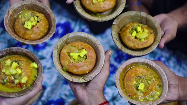 Top-down b-roll footage of multiple hands holding traditional leaf bowls (donas) filled with authentic Indian street food Kachori and Aloo Sabzi, showcasing community eating and festive celebration.
