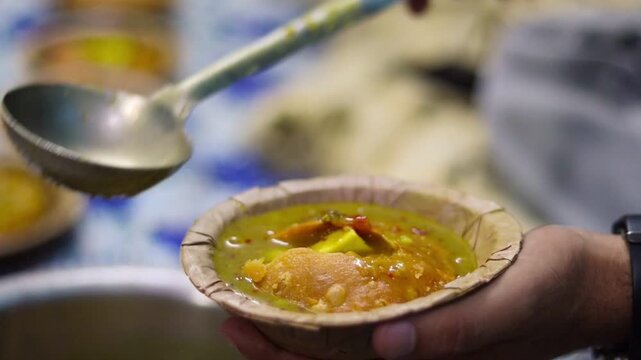 Close-up cinematic b-roll footage of serving hot spicy potato curry over a crushed deep-fried kachori in a traditional leaf bowl (dona), showcasing authentic Indian street food.
