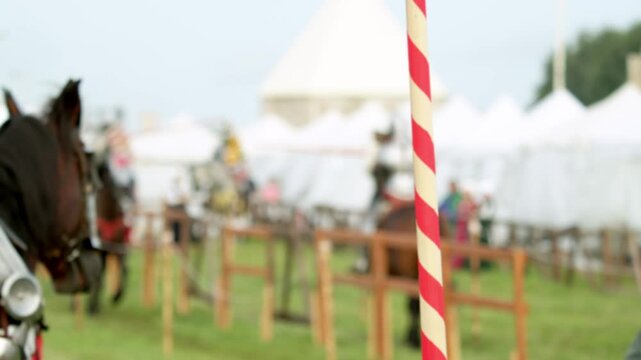 Mounted knights clash violently in blurred background of tournament arena, with wooden lances shattering into splinters upon impact against steel plate breastplates while striped tilt post stands in