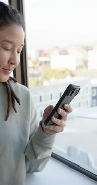 Vertical video: African American non-binary glancing, checking phone text at window, copy space