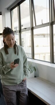 Vertical video: Nonbinary person entering, sitting on window bench, reading smartphone and smiling