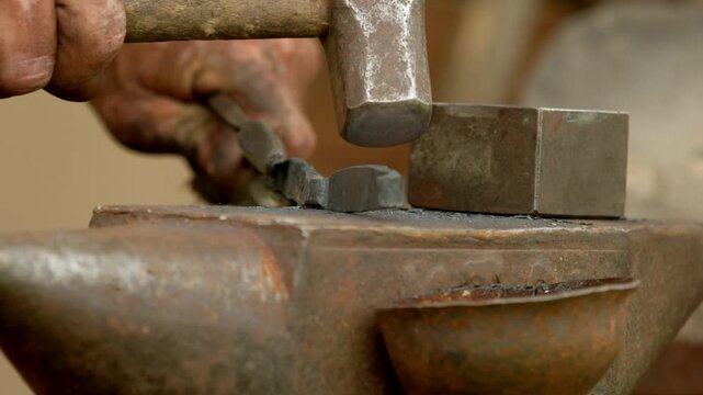 Macro closeup shot captures medieval blacksmith striking hot metal with heavy hammer on cast iron anvil in open-air workshop at historical craft fair.