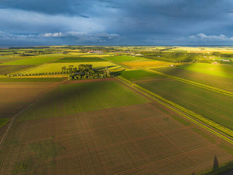 High angle wide horizontal aerial drone photograph of polder fields, farmstead campsite, and dramatic storm sky in Kamperland, Zeeland, Netherlands in golden hour summer light