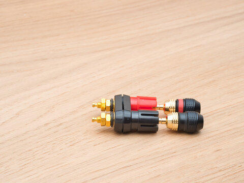 Audio Connectors and Banana Plugs - Close-up of a speaker binding post terminal with red and black banana plugs on a light wooden background, showing audio connection component