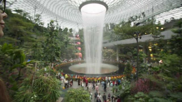 Beautiful tourist enjoying the indoor waterfall at Changi Airport in Singapore with tropical greenery modern biomimetic architecture and travel experiences in Asia