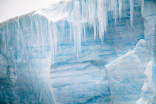 Blue glacier ice wall with hanging icicles