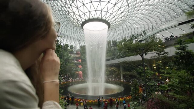 Tourist woman enjoying a walk inside Singapore airport featuring iconic futuristic architecture lush indoor gardens and a breathtaking covered waterfall in Asia