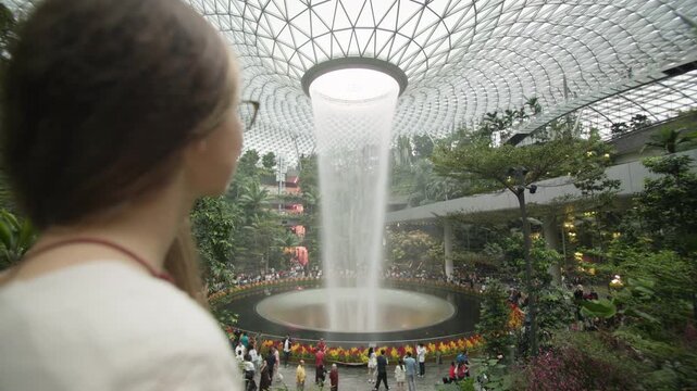 Woman walking through the spectacular Singapore airport interior with futuristic design indoor rainforest gardens and a famous covered waterfall for travel in Asia