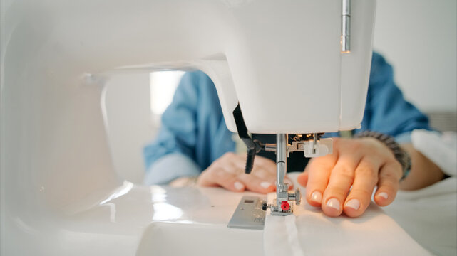 Person guides white fabric under sewing machine needle during bright daytime creative work session