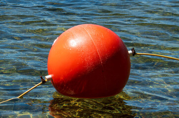 Close-up of a bright red mooring buoy and yellow rope floating in the clear, rippled waters of a lake in McCall, Idaho. © Charles