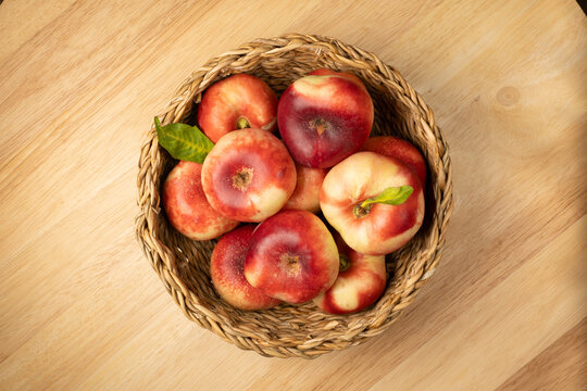 Flat nectarines filling rustic basket on wood table