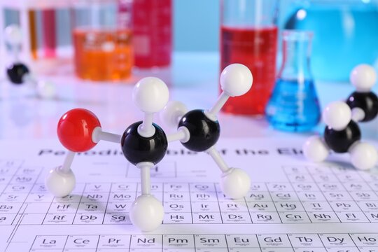 Chemical model of ethanol molecule, periodic table and laboratory glassware on white table, closeup