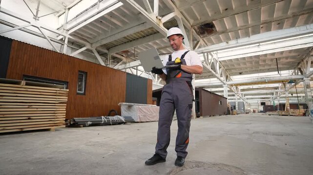 Construction engineer working on laptop at modular home factory