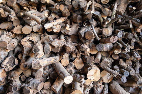 A textured stack of cut dry firewood logs and weathered branches gathered together for fuel
