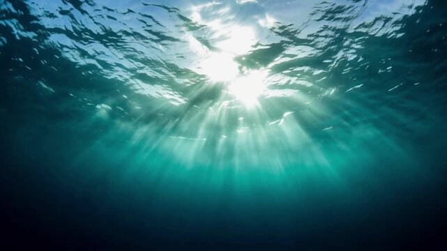 Bright sun rays beaming through clear blue ocean water surface into deep sea, underwater view