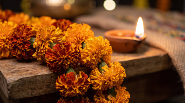 Orange marigold flower garland on wooden table with burning clay oil lamp diya. Diwali festival celebration decoration. Traditional indian hindu ritual with candles and flowers for holiday.