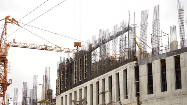 Multi story building under construction with exposed reinforcement bars, concrete structural elements and tower crane, showing reinforced concrete construction and urban development process