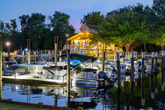 An illuminated waterfront cafe and marina along the waters of the Waccamaw River at early evening seen from the Conway Riverwalk, in the small town of Conway, South Carolina.
