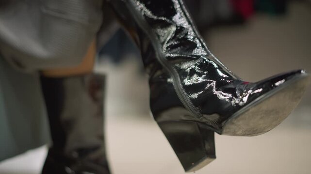 Close up of woman foot wearing shiny black patent leather boots with high heels highlighting reflective surface and stitching details. boot is shown in various positions to emphasize its
