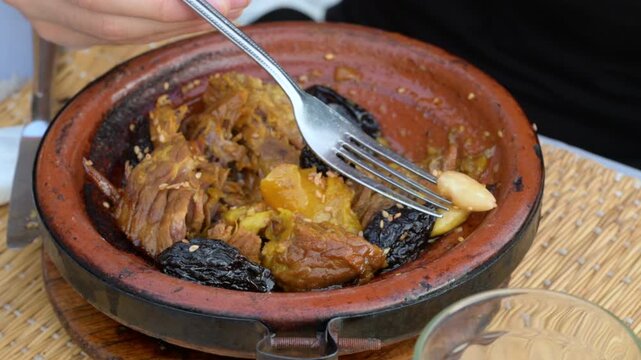 Marrakech, morocco. August 9, 2026. Authentic moroccan cuisine featuring a lamb tagine with prunes and almonds. A person using a fork to eat the tender meat from the clay pot