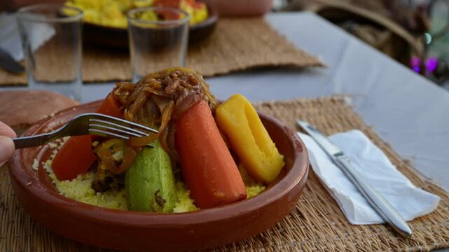 Marrakech, morocco. August 9, 2026. Close up of a person using a fork to eat a traditional moroccan couscous with vegetables, served in a classic terracotta tagine dish